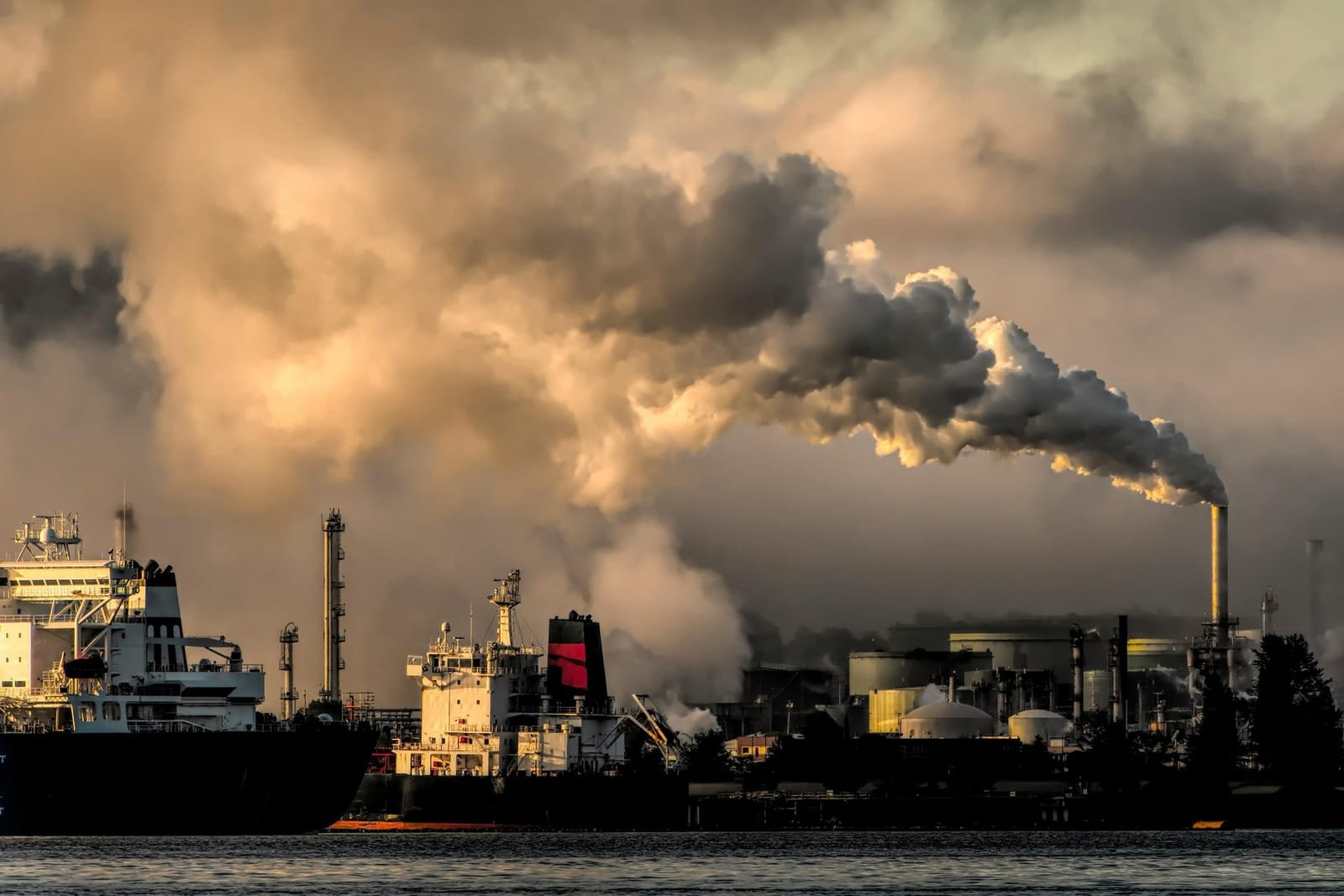 An industrial waterfront under a heavy smoke plume at dusk